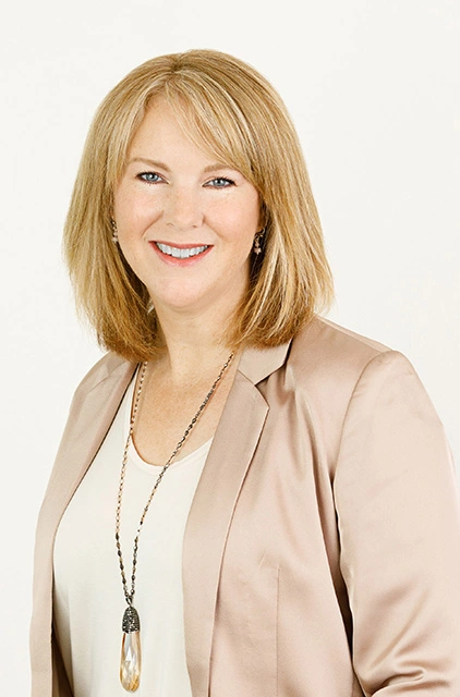 A woman in a beige jacket and white shirt.